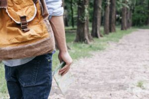 midsection-traveler-man-holding-map-carrying-backpack-outdoors