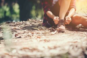 Young woman hiker stops to tie her shoe on a summer hiking trail in forest.